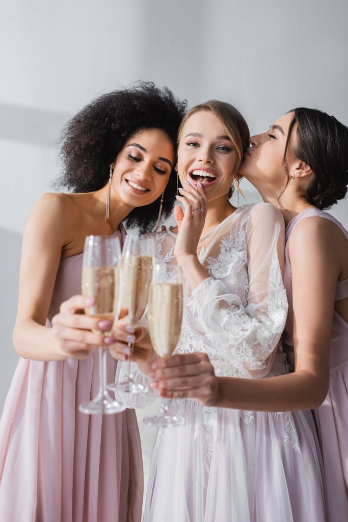 взволнованная невеста смотрит в камеру во время звона бокалов шампанского с мультикультурными друзьями - Фото, изображение