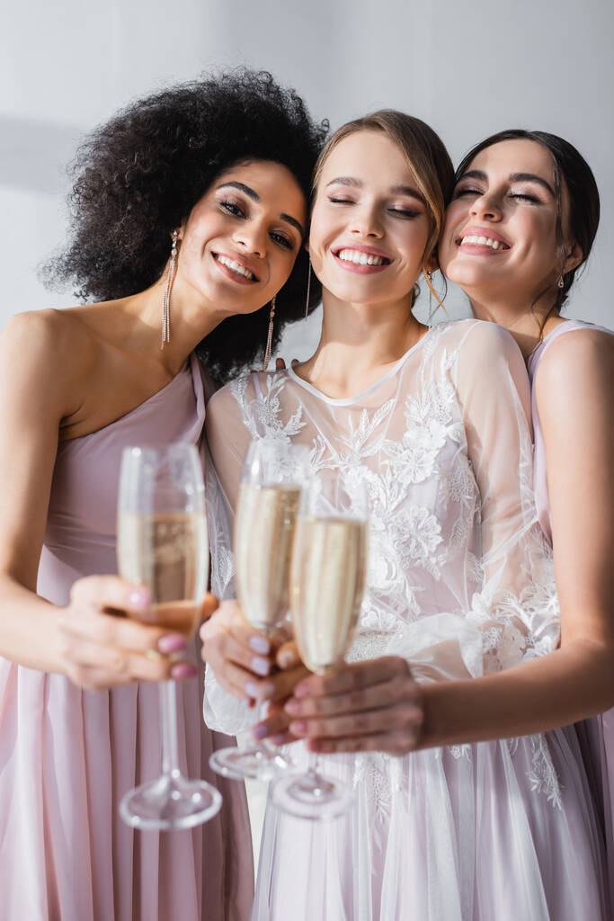 cheerful bride with bridesmaids clinking champagne glasses on blurred foreground - Photo, Image