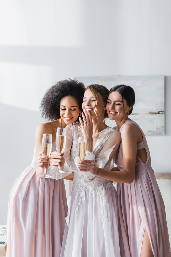excited bride laughing with closed eyes near interracial bridesmaids holding champagne - Photo, Image