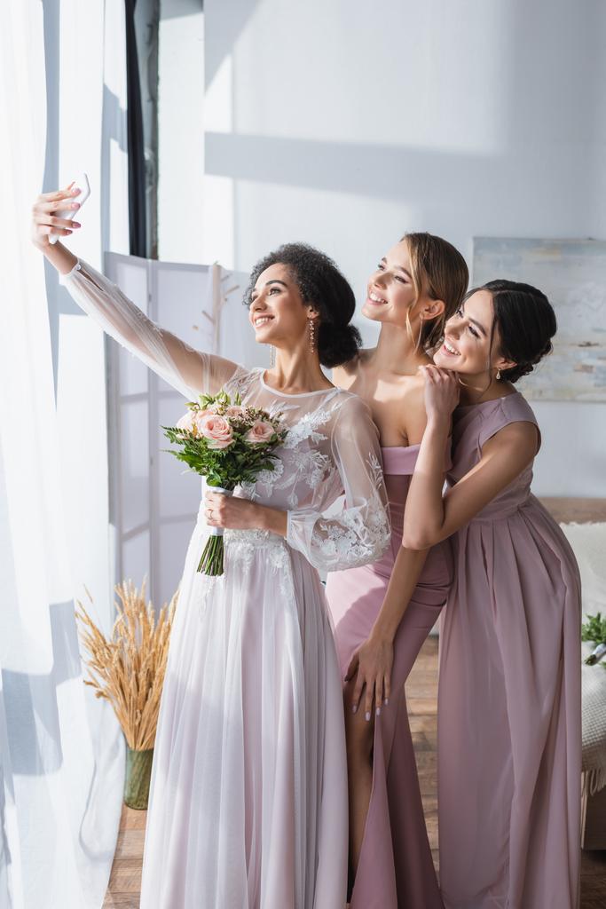 elegante afrikanisch-amerikanische Braut macht Selfie mit hübschen Freundinnen im Schlafzimmer - Foto, Bild