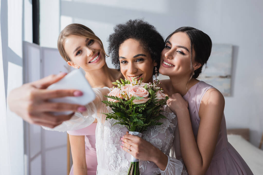 mariée afro-américaine prenant selfie avec bouquet de mariage et demoiselles d'honneur, premier plan flou - Photo, image