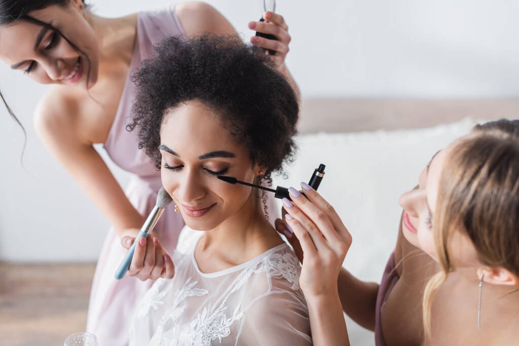 smiling women doing makeup to pretty african american bride, blurred background - Photo, Image