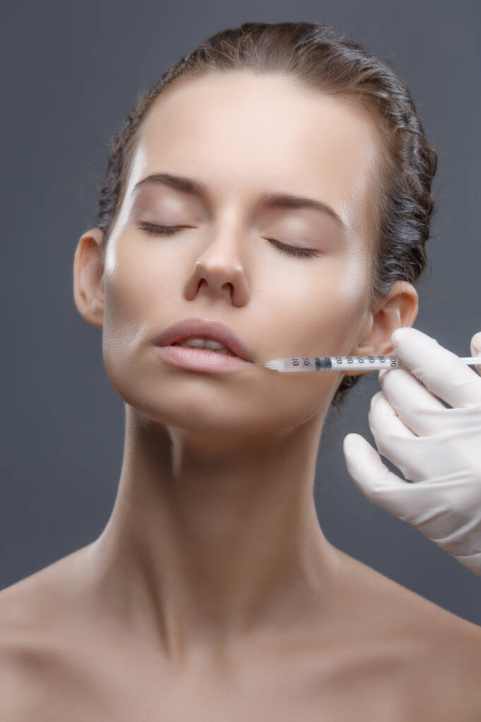 De arts cosmetoloog maakt de Verjongende gezichtsinjecties procedure voor aanscherping en gladstrijken rimpels op de gezichtshuid van een vrouw in een schoonheidssalon. Cosmetologie huidverzorging - Foto, afbeelding