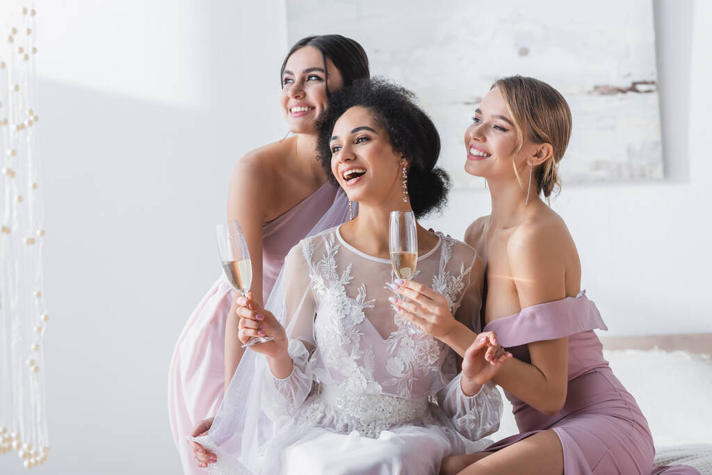 excited african american bride holding champagne near happy bridesmaids - Photo, Image