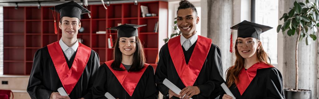 szczęśliwy międzyrasowy studenci w suknie i czapki z dyplomem, bal 2021, sztandar - Zdjęcie, obraz
