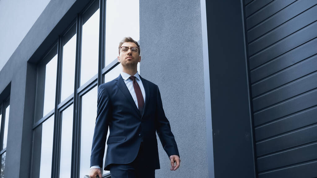 Selbstbewusster Geschäftsmann in Anzug und Brille geht in Baunähe  - Foto, Bild