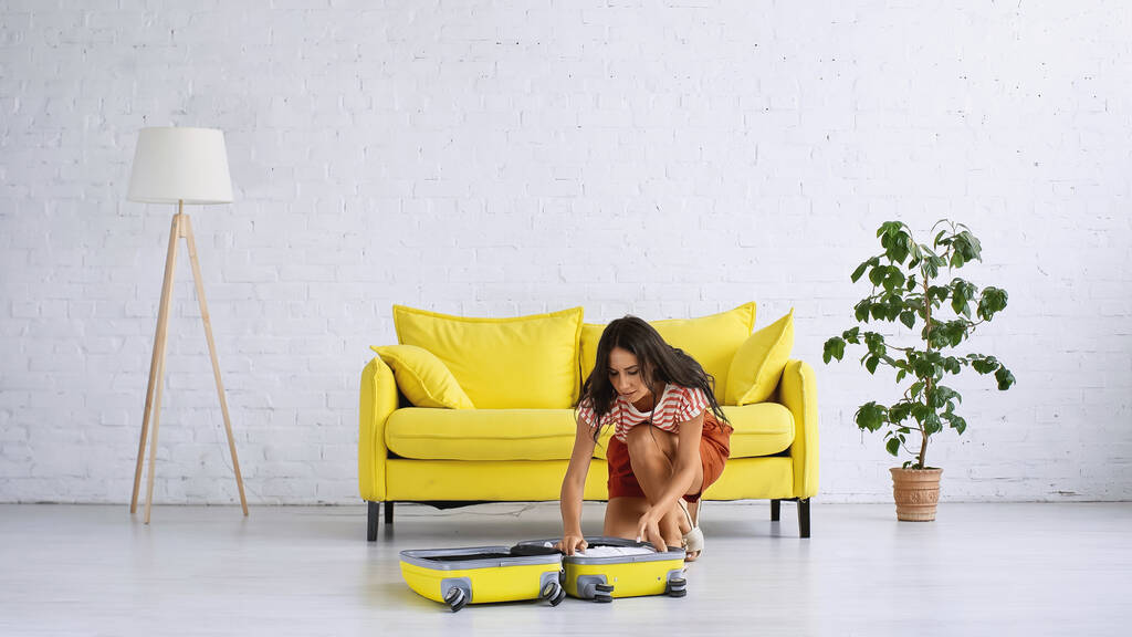 barna nő ül közelében sárga bőrönd és kanapé a nappaliban - Fotó, kép