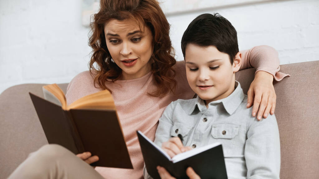 Madre e hijo haciendo deberes con libro y cuaderno en casa  - Foto, Imagen