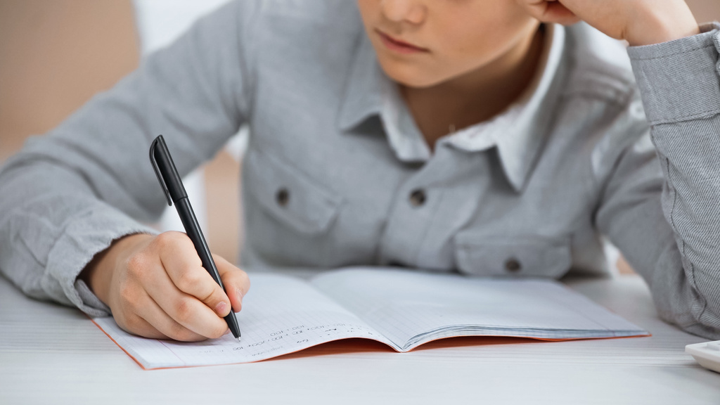 Gesneden weergave van jongen schrijven op kopieerboek thuis  - Foto, afbeelding
