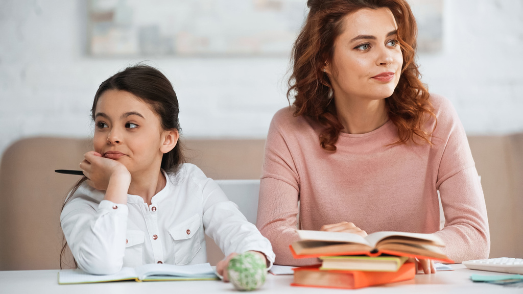 Displeased daughter and mother looking away near books on table  - Photo, Image