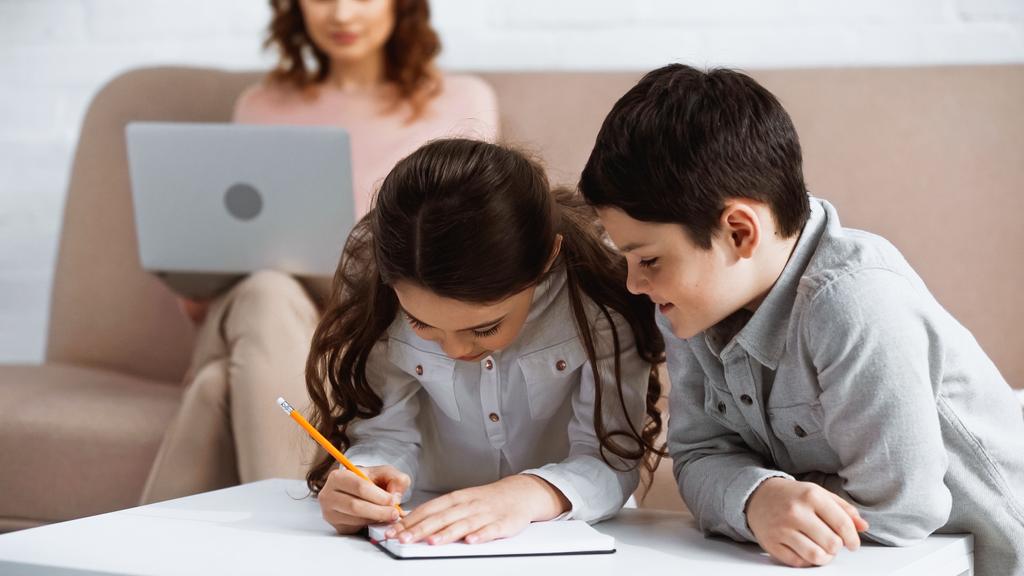 Дети делают домашнее задание на ноутбуке рядом с матерью с ноутбуком на размытом фоне  - Фото, изображение