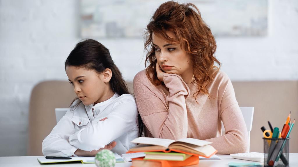 Woman looking at dissatisfied daughter with crossed arms near books  - Photo, Image