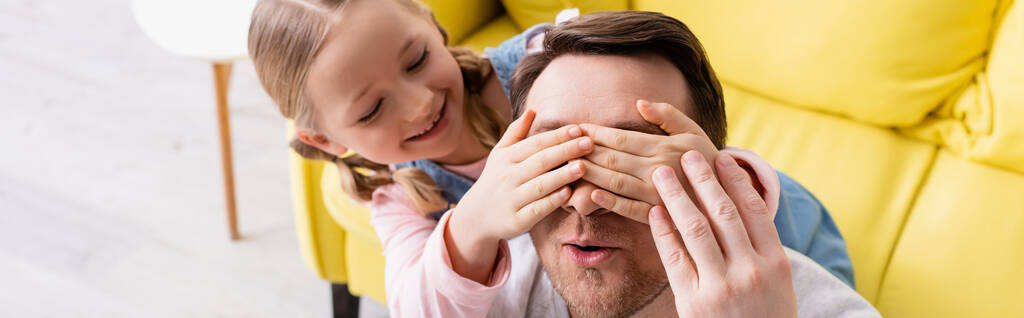 χαρούμενο παιδί που καλύπτει τα μάτια του έκπληκτου πατέρα ενώ διασκεδάζει στο σπίτι, banner - Φωτογραφία, εικόνα