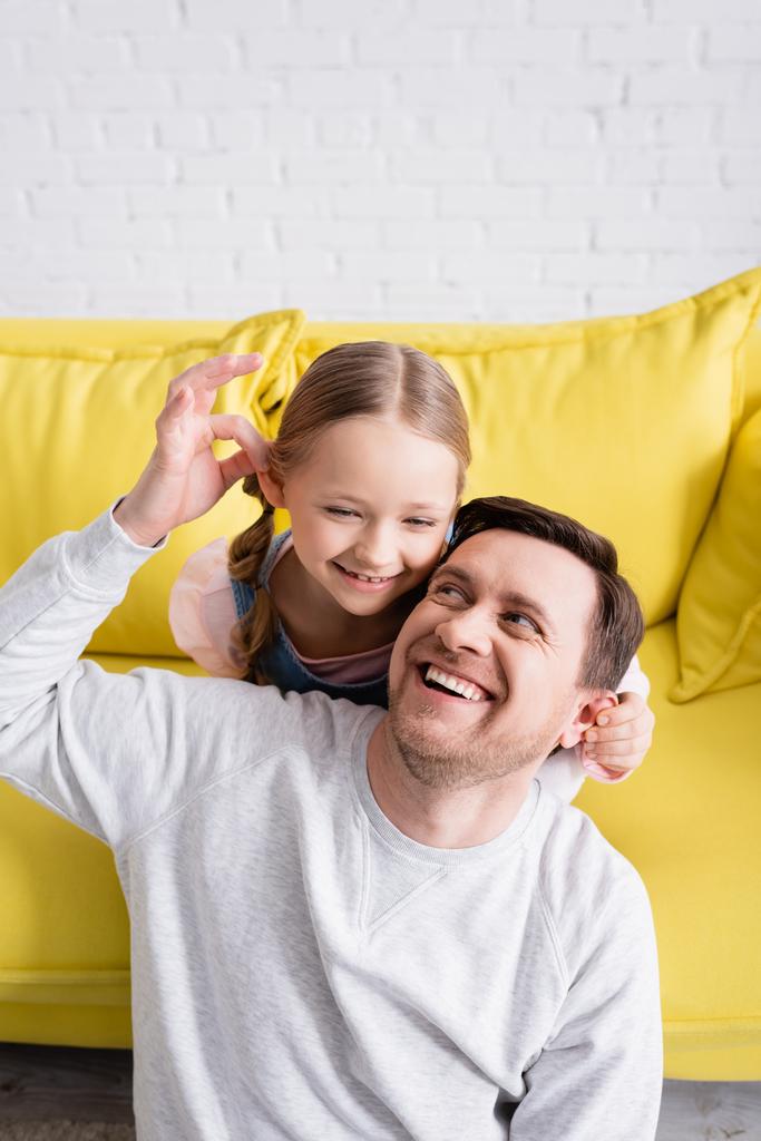 веселая девушка и смеющийся отец трогают уши друг друга, веселясь дома - Фото, изображение