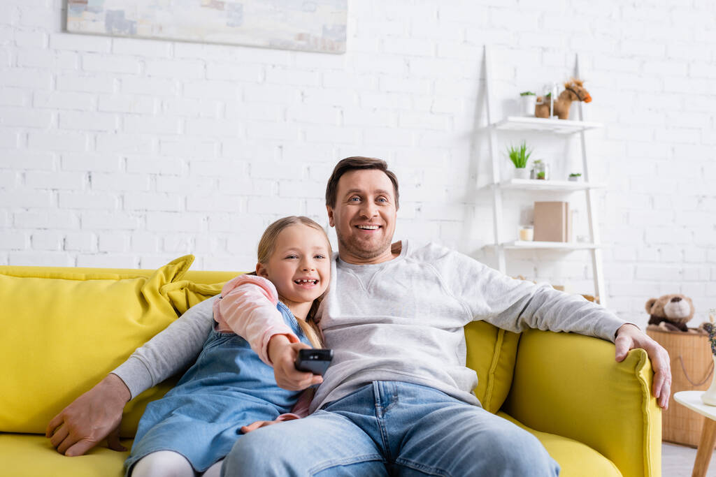homme souriant regarder la télévision avec fille en cliquant sur les canaux sur la télécommande - Photo, image