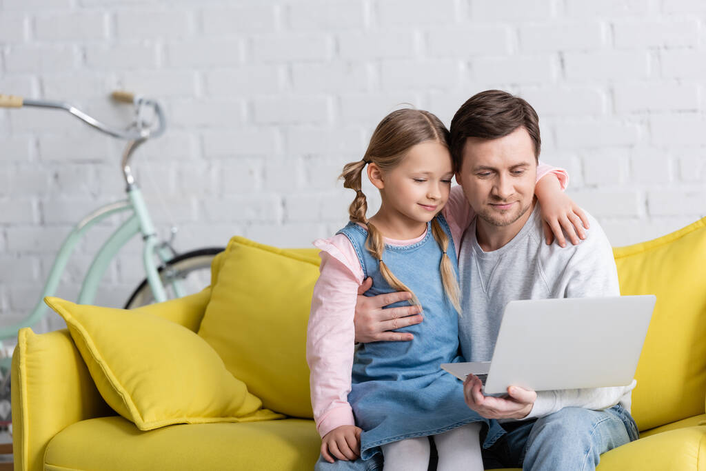 улыбающиеся отец и ребенок смотрят фильм на ноутбуке дома - Фото, изображение