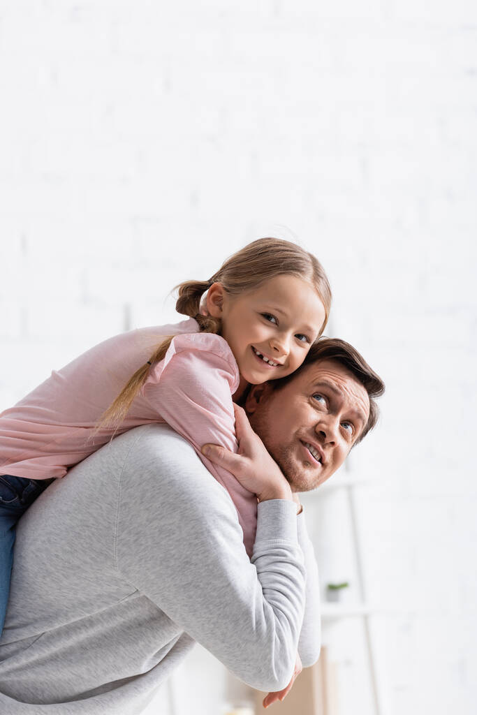 sonriente hombre piggybacking feliz hija en casa - Foto, imagen