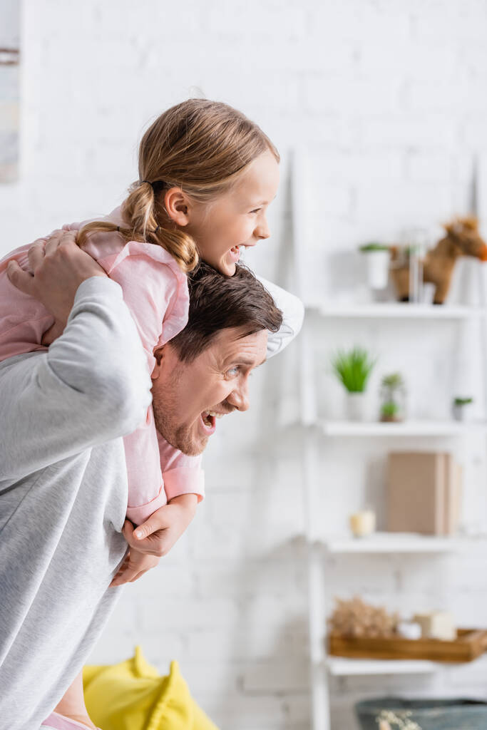 alegre hombre piggybacking sorprendido hija mientras se divierten en casa - Foto, imagen