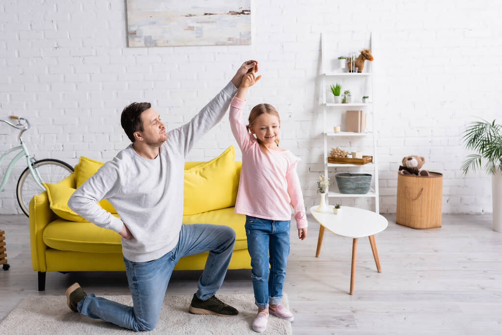 hombre de pie sobre la rodilla mientras baila con su hija en casa - Foto, imagen