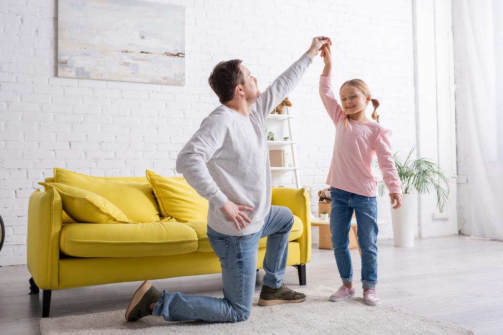 happy girl having fun while dancing with father standing on knee at home - Photo, Image