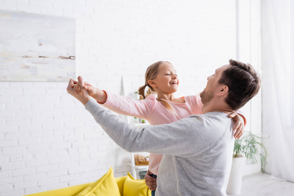 мужчина держит радостную дочь и танцует дома - Фото, изображение