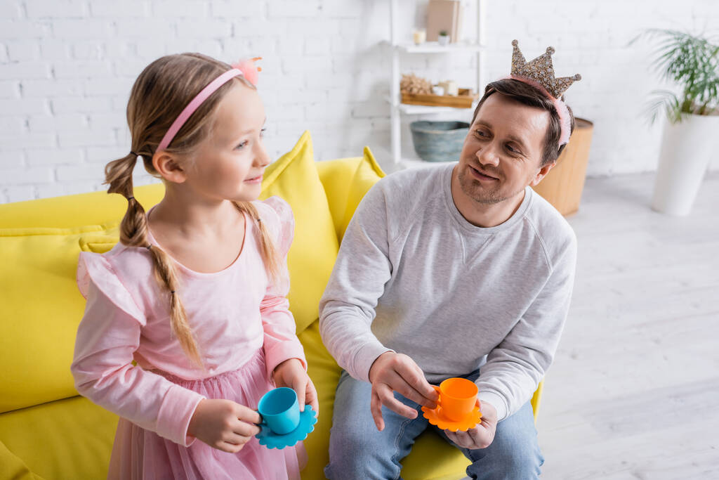 souriant père et fille tenant des tasses de jouets tout en jouant à la maison - Photo, image