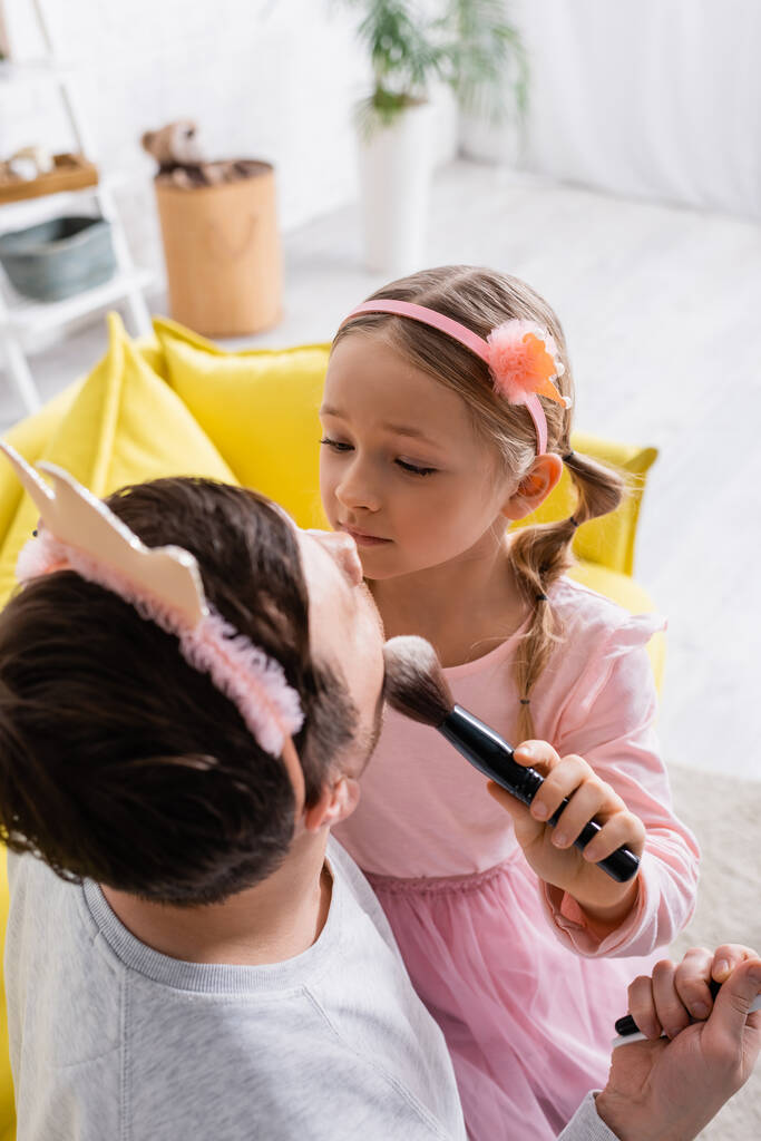 visão de alto ângulo da menina em coroa de brinquedo fazendo maquiagem para o pai em primeiro plano desfocado - Foto, Imagem