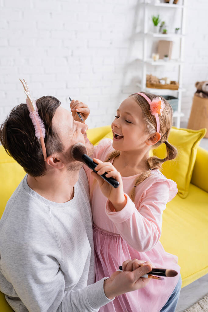 alegre hija aplicando maquillaje a padre usando juguete corona - Foto, Imagen