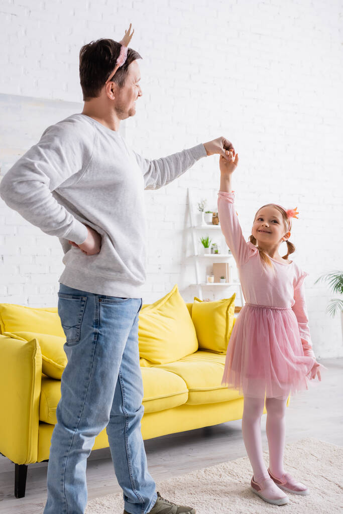 adult man in toy crown holding hand on hip while dancing with daughter - Photo, Image