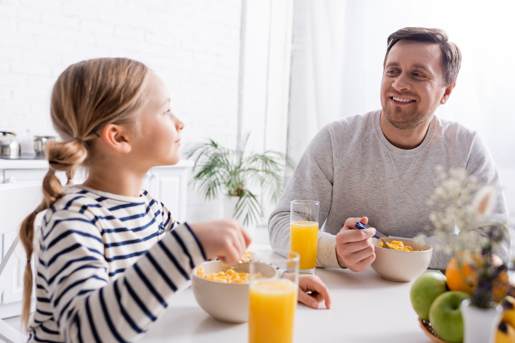Ευτυχισμένος πατέρας και κόρη κοιτάζονται κατά τη διάρκεια του πρωινού στην κουζίνα - Φωτογραφία, εικόνα