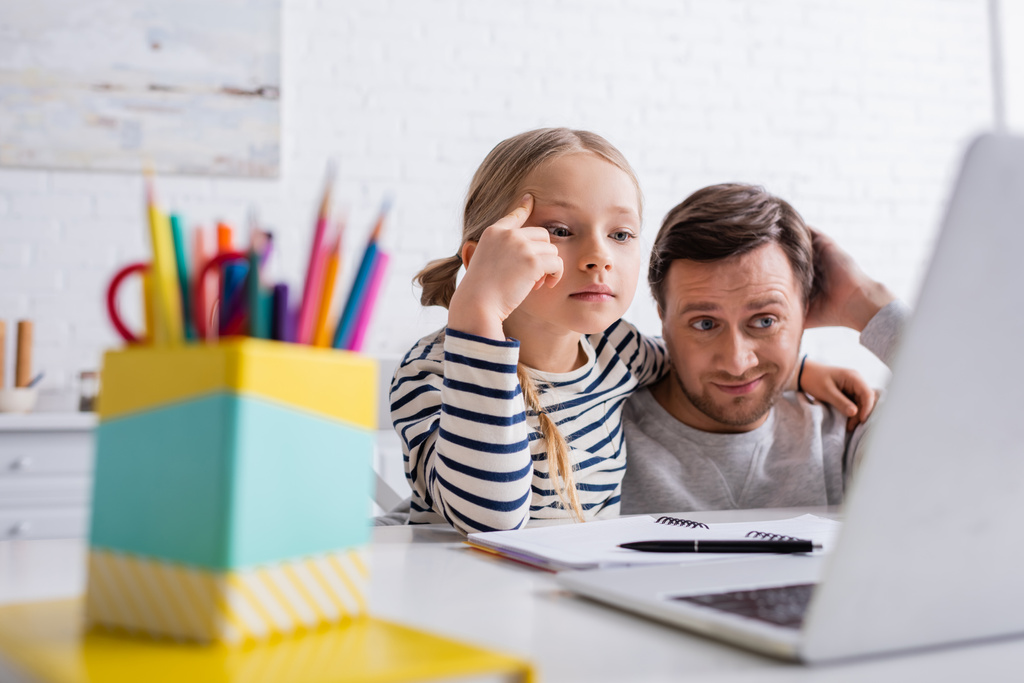 Düşünceli baba ve kız online ön plan bulanıklığı dersi sırasında dizüstü bilgisayara bakıyorlar. - Fotoğraf, Görsel