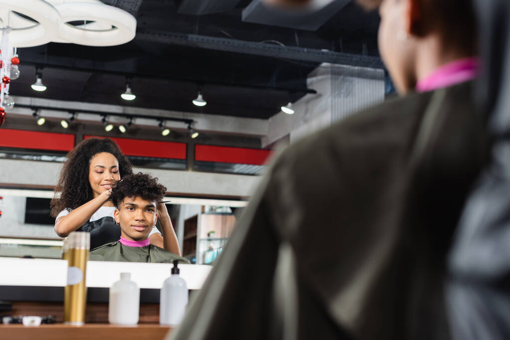 Gülümseyen Afro-Amerikan kuaför bulanık ön planda müşterinin yanında duruyor.  - Fotoğraf, Görsel