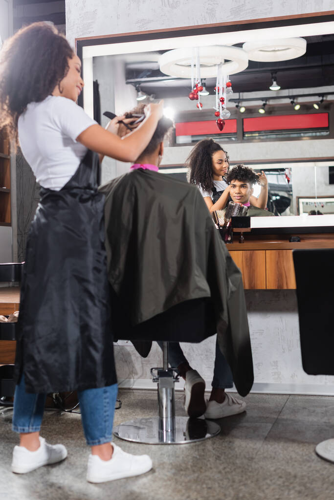 Afrykański amerykański fryzjer strzyżenie włosów klienta na zamazanym pierwszym planie w salonie  - Zdjęcie, obraz