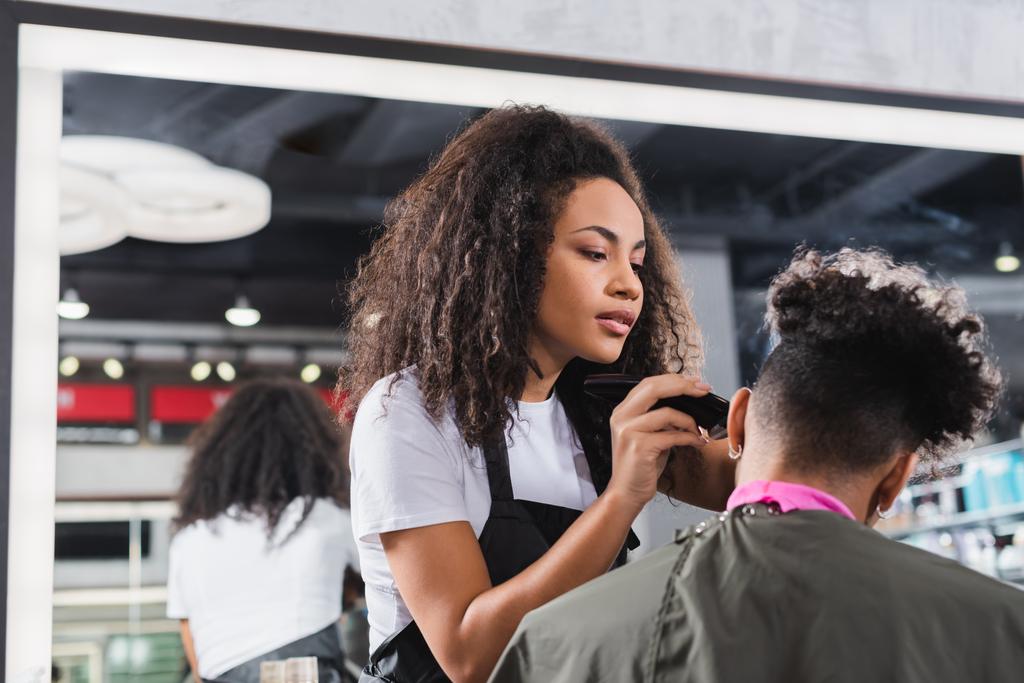 Genç Afrikalı Amerikalı kuaför kıvırcık müşterinin saçını kesiyor.  - Fotoğraf, Görsel
