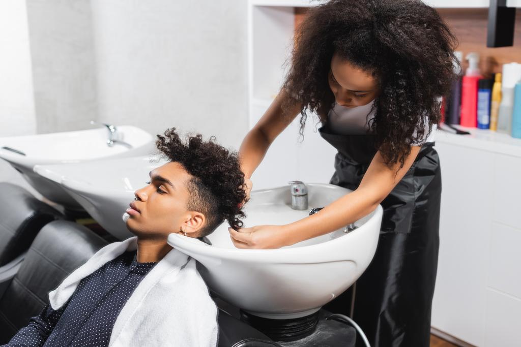 Afrikalı Amerikalı kuaför havluyla adam saçı yıkıyor.  - Fotoğraf, Görsel
