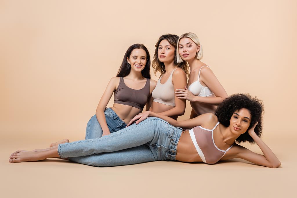 african american woman in bra and jeans lying near interracial friends on beige - Photo, Image