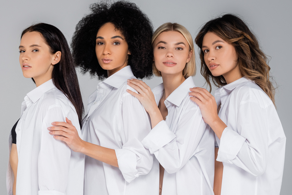 jong interraciaal vrouwen in wit shirts kijken naar camera op grijs - Foto, afbeelding