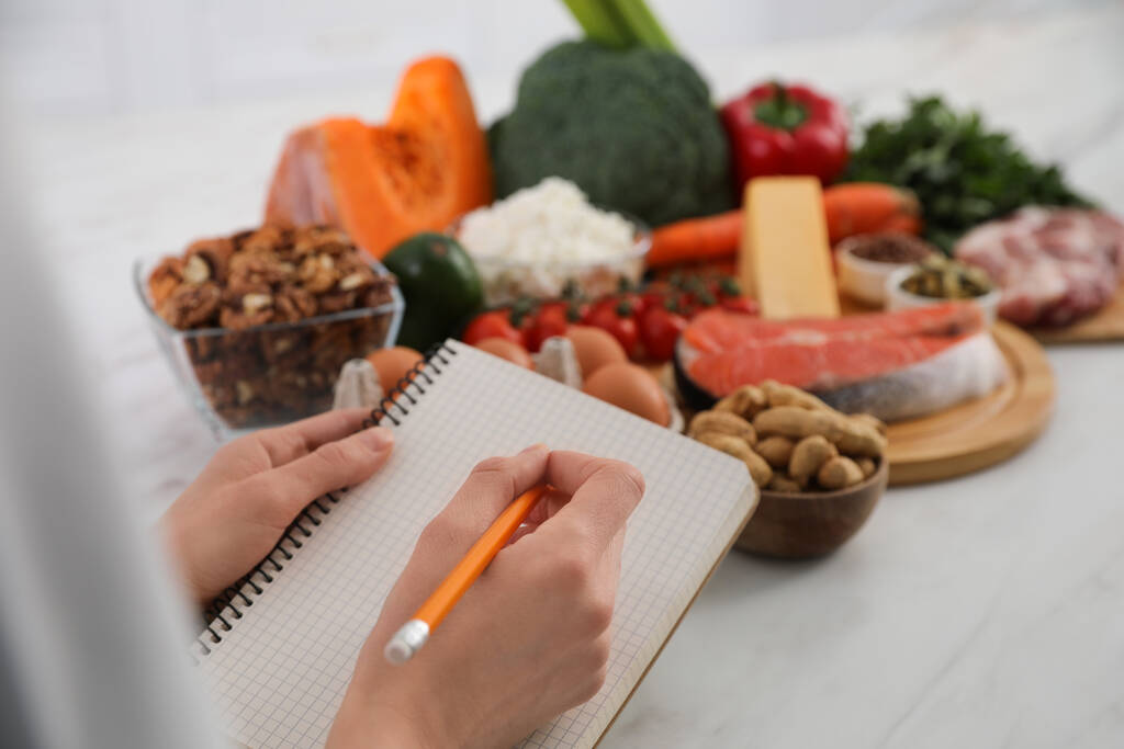 Mujer con cuaderno y comida sana en mesa blanca, primer plano. Dieta Keto - Foto, imagen