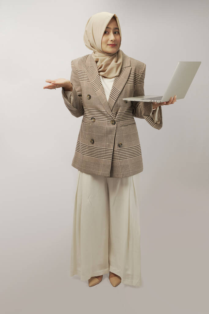  joven musulmana empleada mujer en hijab celebrar y trabajar en el ordenador portátil aislado en fondo de pared blanca, retrato de estudio. Concepto de estilo de vida religioso. Simular espacio de copia - Foto, imagen