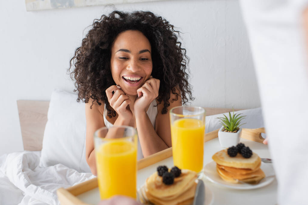 мужчина держит поднос с завтраком рядом счастливая африканская американская подруга  - Фото, изображение