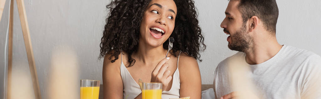 vousatý muž při pohledu na africké americké přítelkyně jíst ostružiny, banner - Fotografie, Obrázek