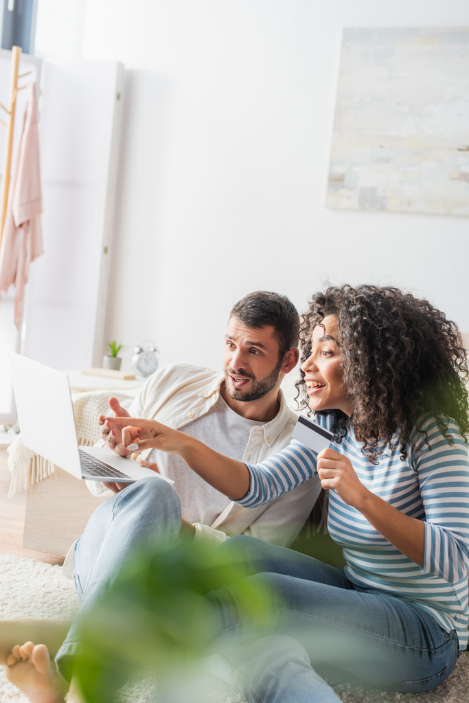 excité interracial couple shopping en ligne tout en utilisant ordinateur portable dans la chambre à coucher avec flou premier plan  - Photo, image