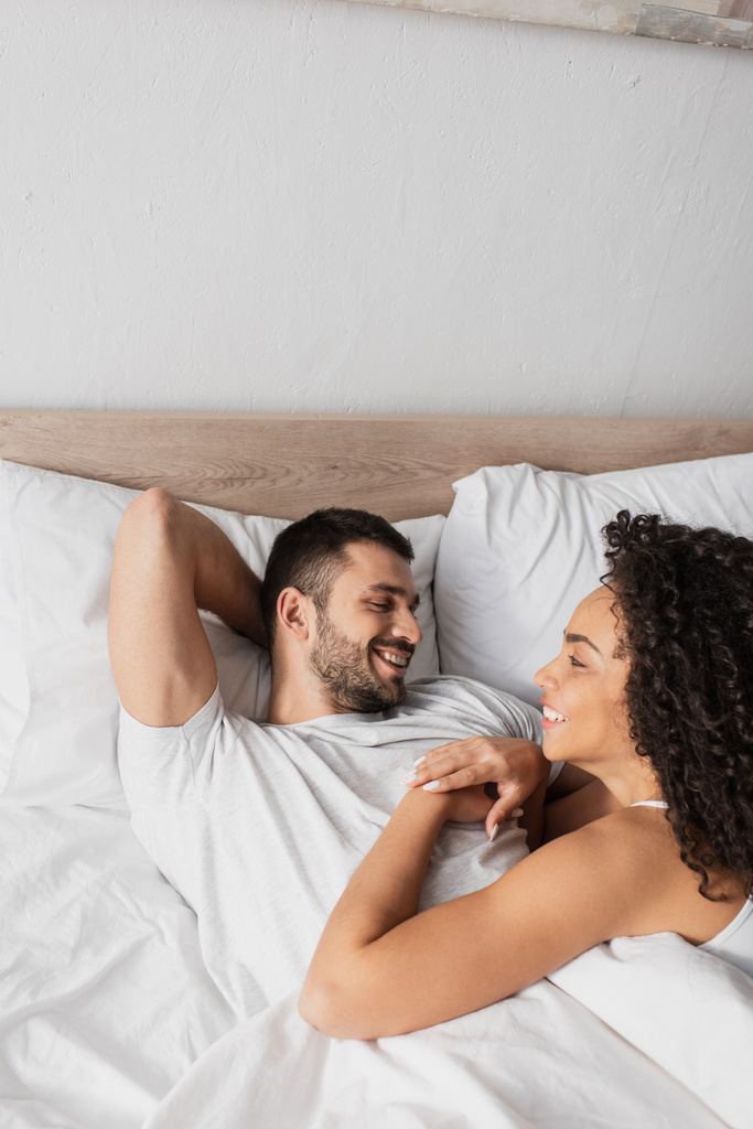 felice coppia interrazziale guardando l'un l'altro a letto  - Foto, immagini