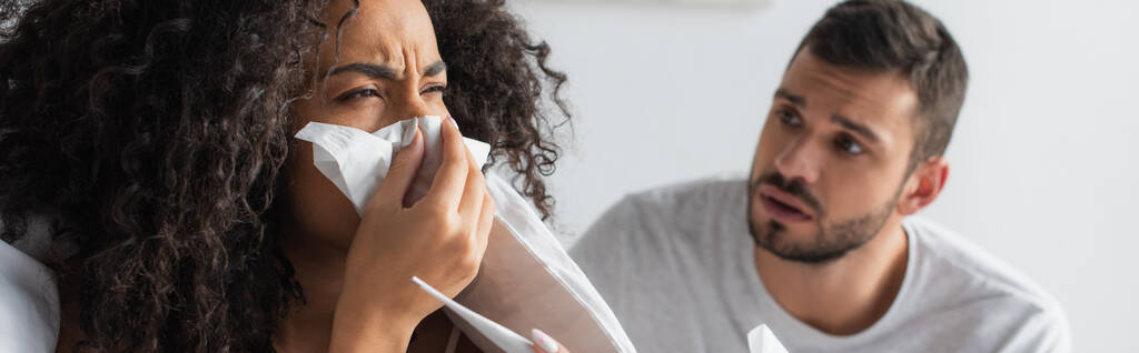 sick african american woman sneezing in napkin near worried boyfriend, banner - Foto, afbeelding