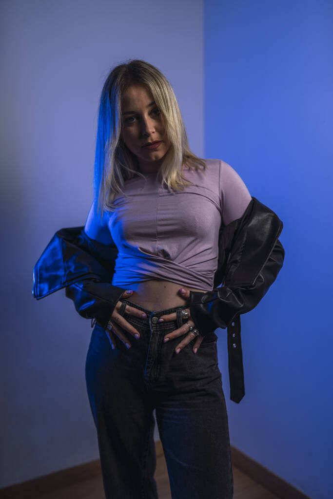 An attractive Caucasian female from Spain in a leather jacket posing in a studio with blue lights - Foto, Imagen