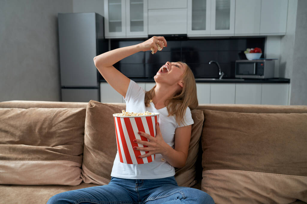 Жінка сидить на дивані і їсть попкорн
 - Фото, зображення