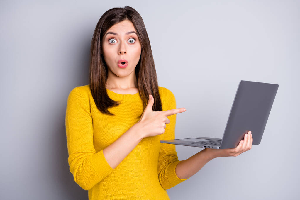 Zdjęcie pod wrażeniem brunetka miła pani trzymać punkt laptop nosić żółty sweter izolowany na szarym tle kolor - Zdjęcie, obraz