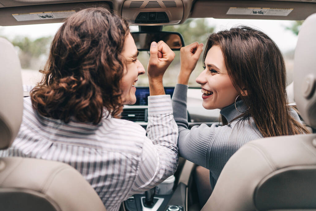 Fröhliches junges Paar vor dem Auto, zu Musik tanzend, einander anschauend, luxuriöser Innenraum. - Foto, Bild