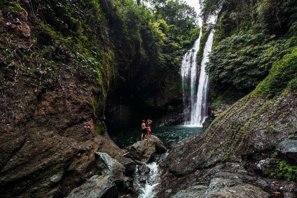 Любителі водоспаду, задній вид. Пара милується прекрасним водоспадом в Індонезії. Пара у відпустці на Балі. Поїздка на медовий місяць. Пара подорожує в Азії. Відпустка на острові Балі - Фото, зображення