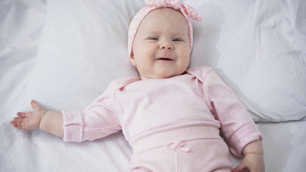 vista dall'alto di sorridente neonata in fascia sdraiata su biancheria da letto bianca - Foto, immagini